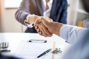 Couple making sign contract then shaking hand with agent in office of property company.